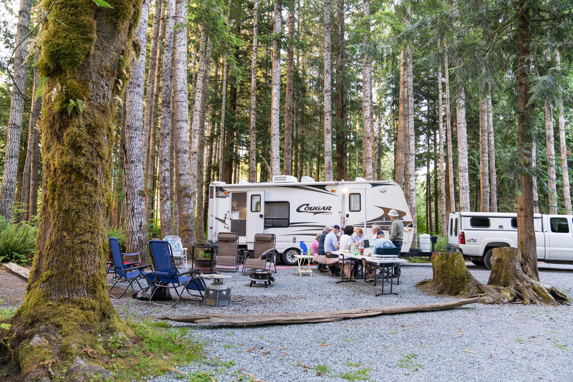A family sits at a picnic table outside of their RV in the redwoods