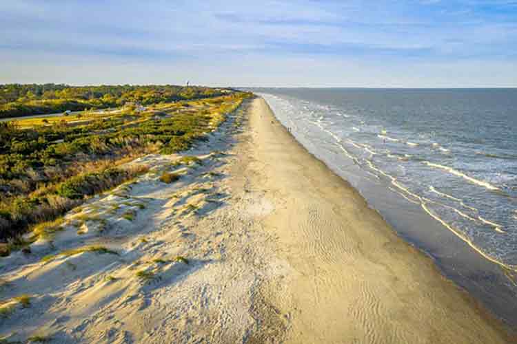 A long stretch of empty sandy beach and ocean view with a water tower in the distance