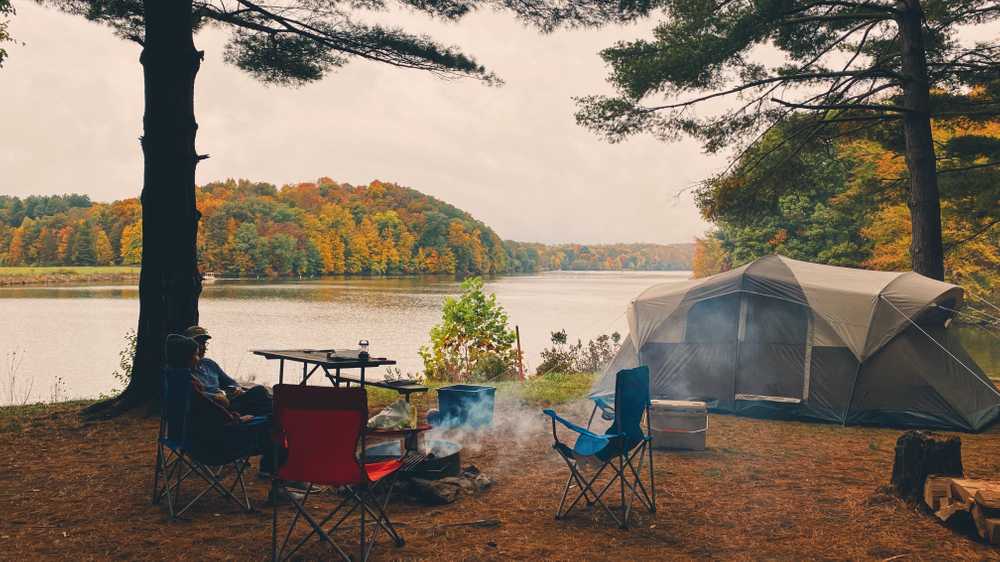 A tent campsite on the edge of a lake surrounded by fall foliage.