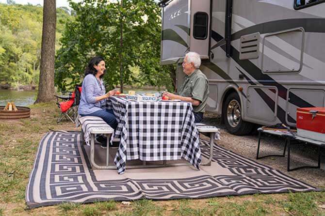 An older couple sit at a picnic table with gingham tablecloth outside of their RV