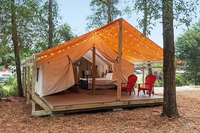 A open glamping tent in the woods with string lights and red Adirondack chairs near the entrance
