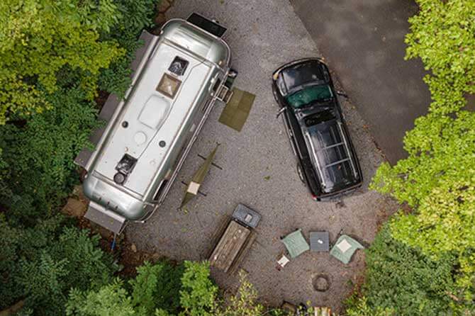 An aerial shot of the top of an Airstream trailer and truck parked at a campsite in the woods