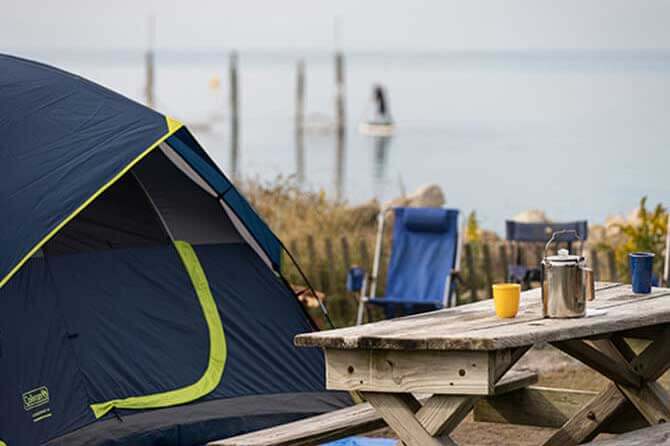 A blue tent next to a picnic table with water views in the backdrop