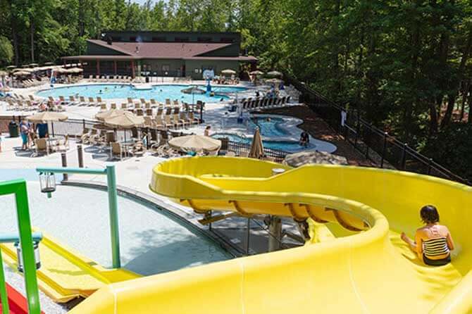 A child rides a yellow water slide to a pool with other campers in the distance