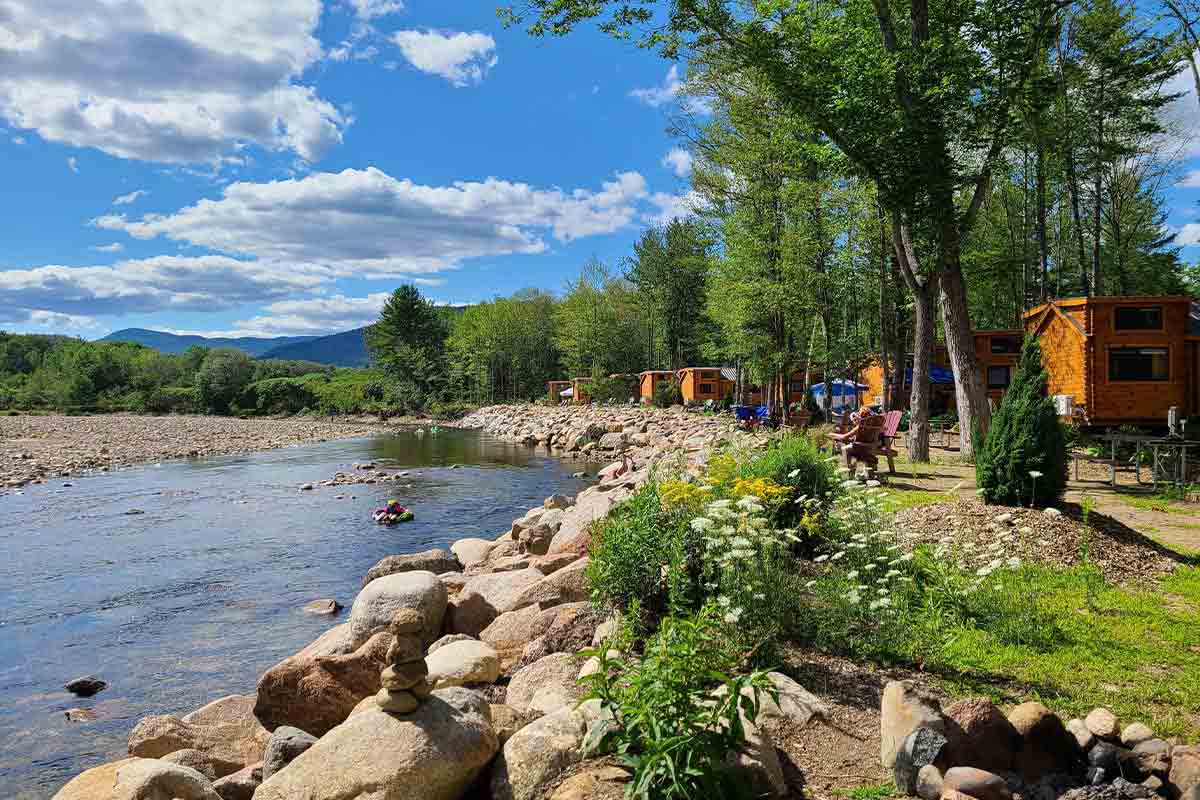 Campground cabins line a body of water with spring wildflowers in the foreground and blue skies and clouds overhead