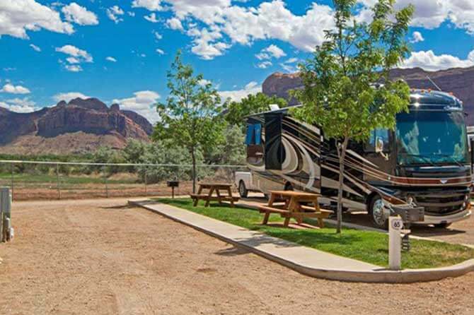 An RV parked at a campsite at Sun Outdoors Arches Gateway in Moab with blue skies and clouds overhead