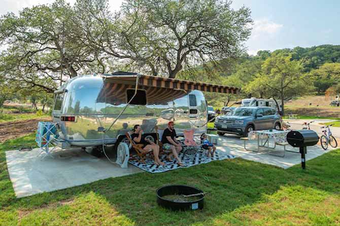 RV parked in campsite at Camp Fimfo Texas Hill Country with trees and rolling hills.