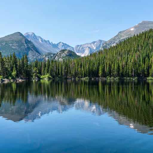 Mountains and trees are reflected in a body of blue water