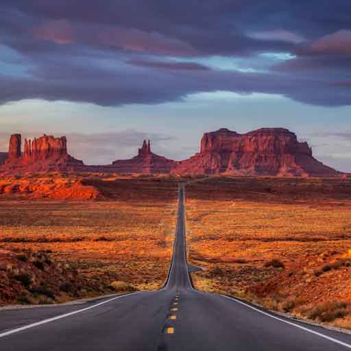 An empty road leads to massive desert rock formations in the distance