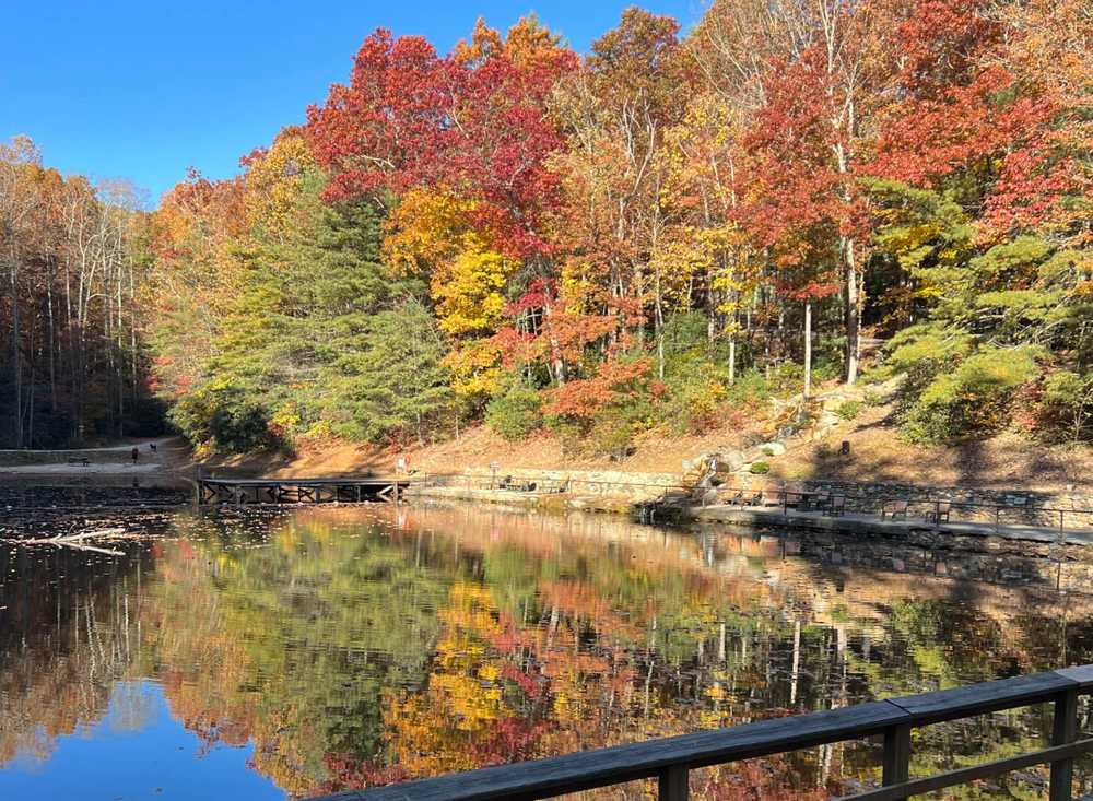 Trees full of fall foliage surround a calm body of water that reflects the colors of the trees.