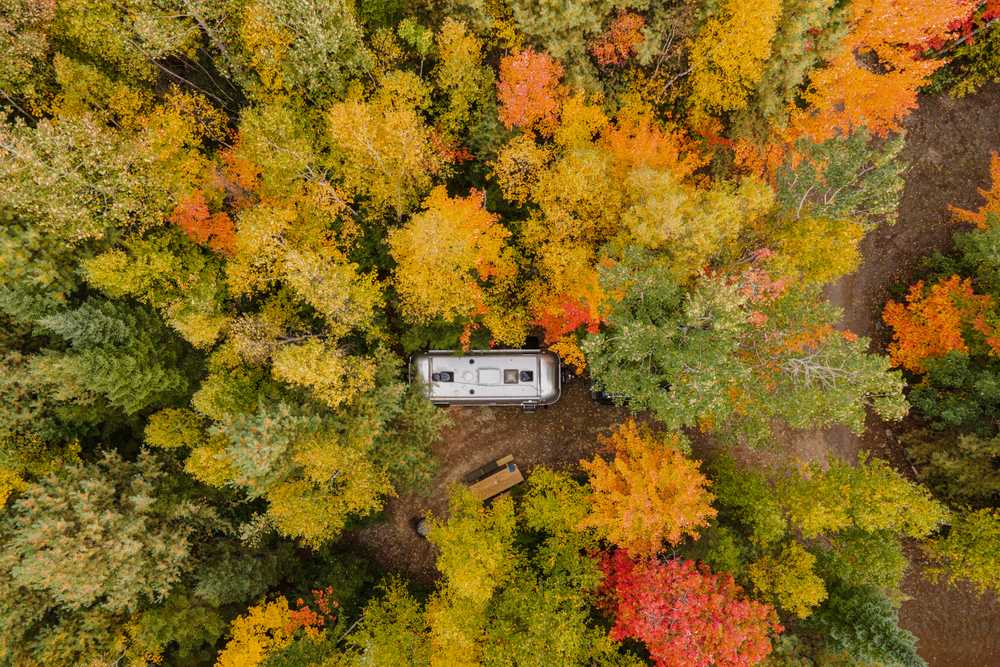 An aerial view of an Airstream trailer in the woods surrounded by fall foliage.