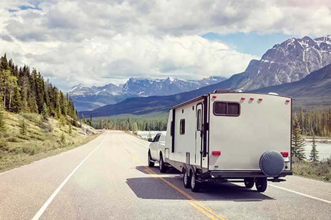 A truck pulls a camper down a road with trees and mountain views in the backdrop
