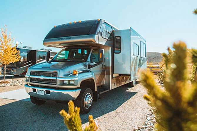 A camper parked in a RV site under blue skies with yellow trees nearby