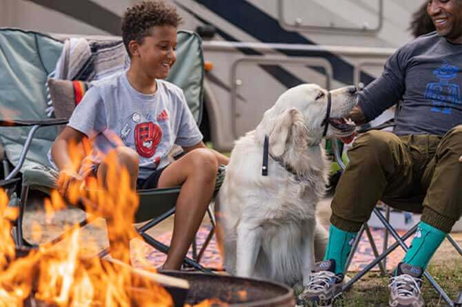 A child sits next to an English cream golden retriever near the fireplace at an RV camping site at one of the best campgrounds for pet lovers