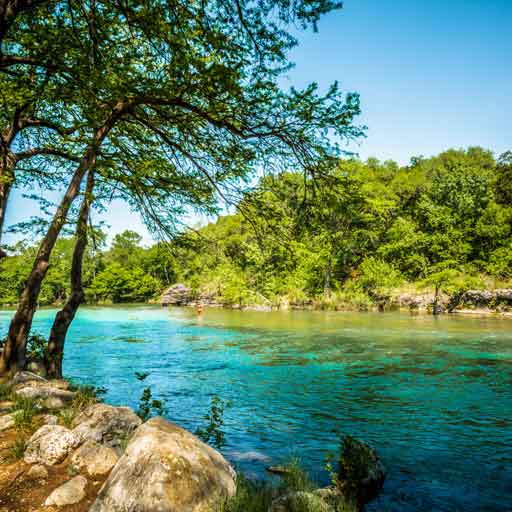 Trees surround a blue-green river near a Texas campground